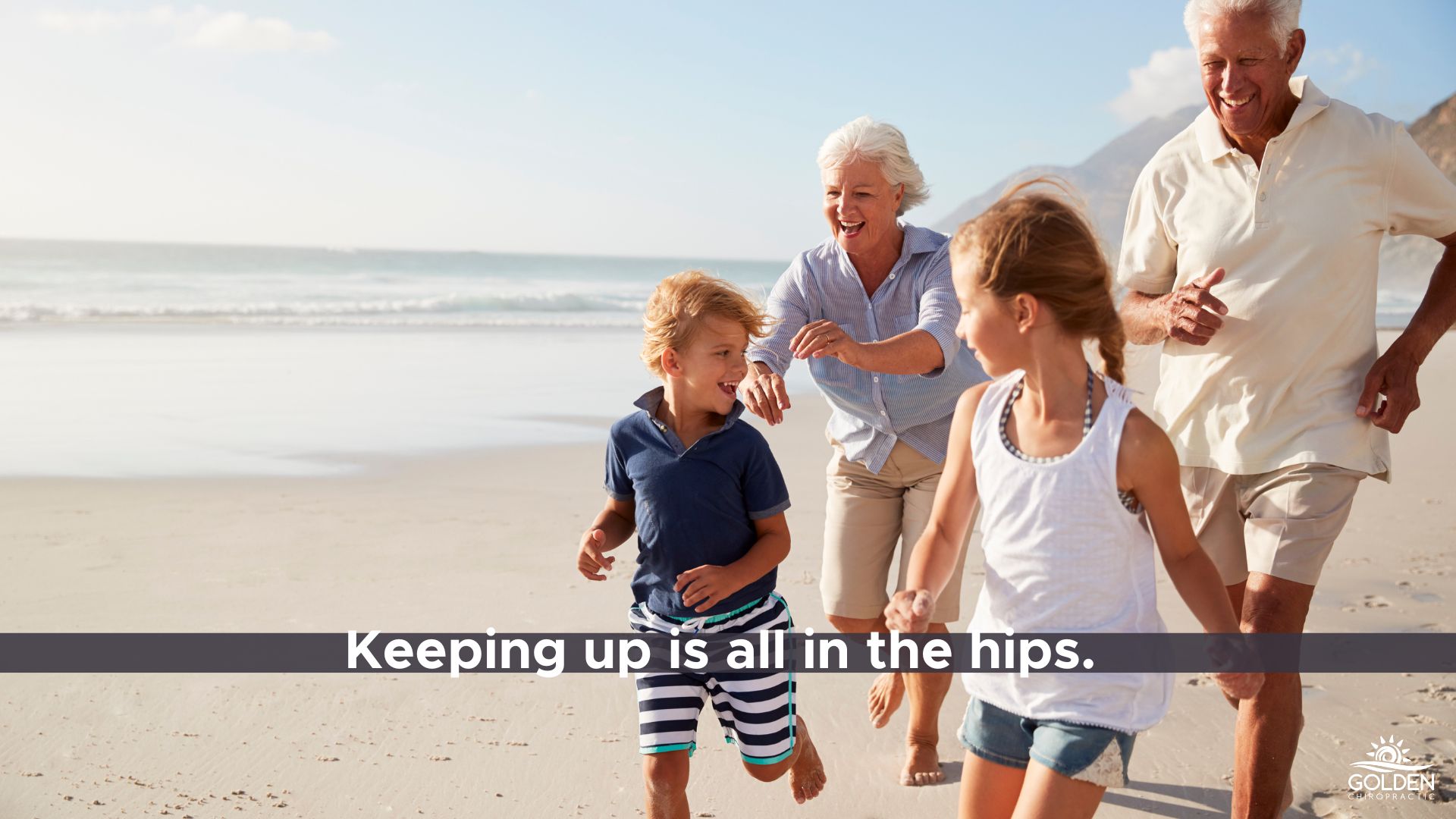 Grandparents chasing young grandchildren along the beach having fun