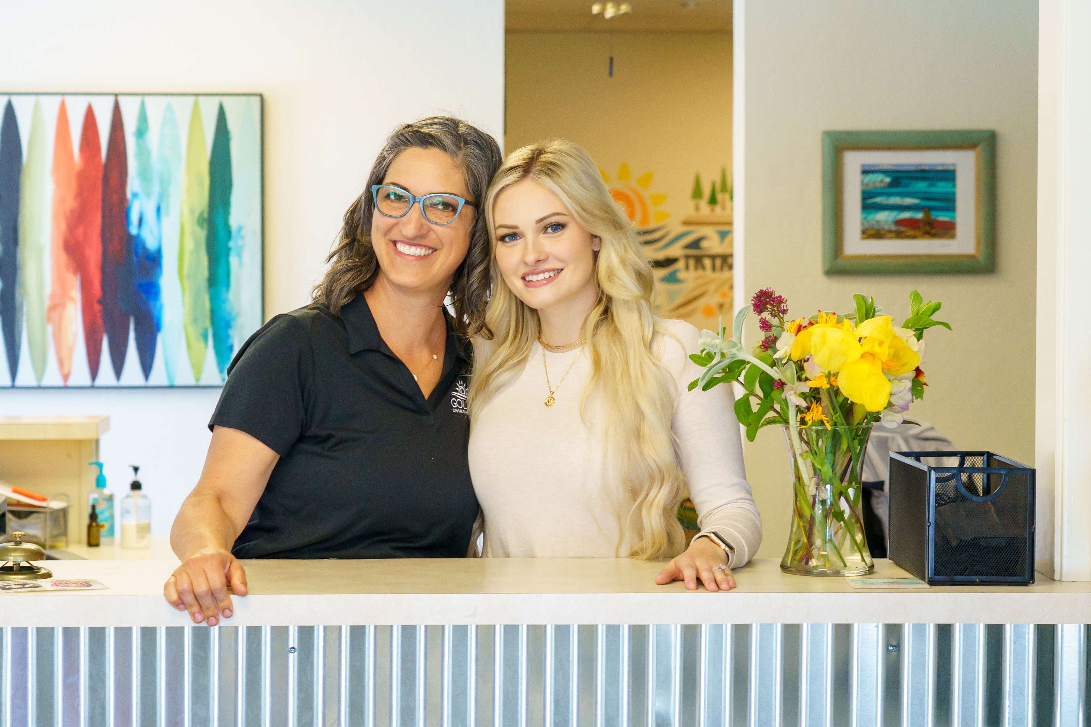 Dr.Goldi and Dr. Michaela standing behind the counter in the front office smiling at the camera