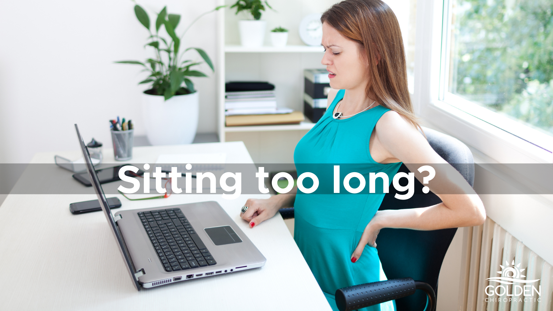 woman sitting at a computer, wincing with her hand on her lower back