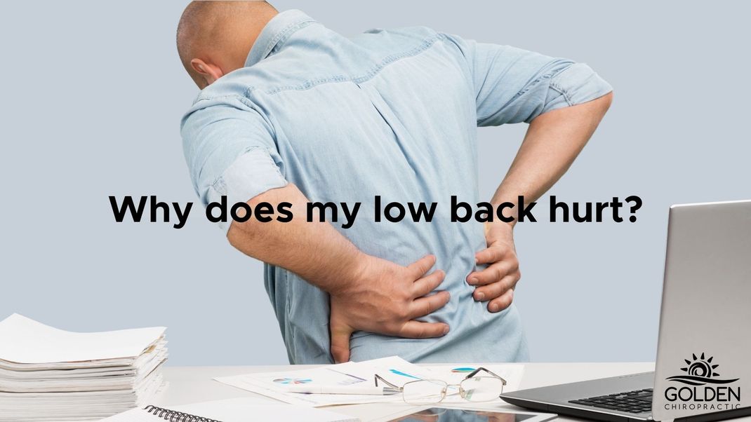 Man clutching his lower back in pain while standing up from his desk