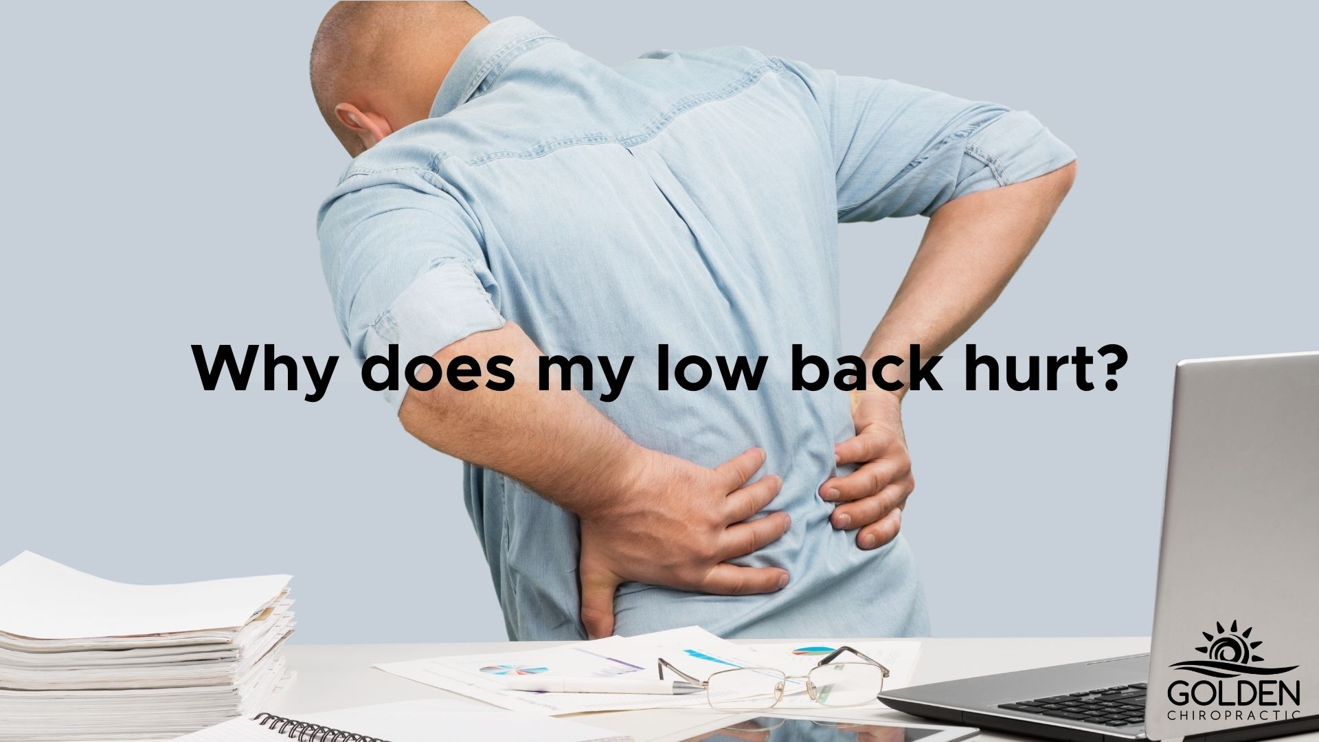 Man clutching his lower back in pain while standing up from his desk