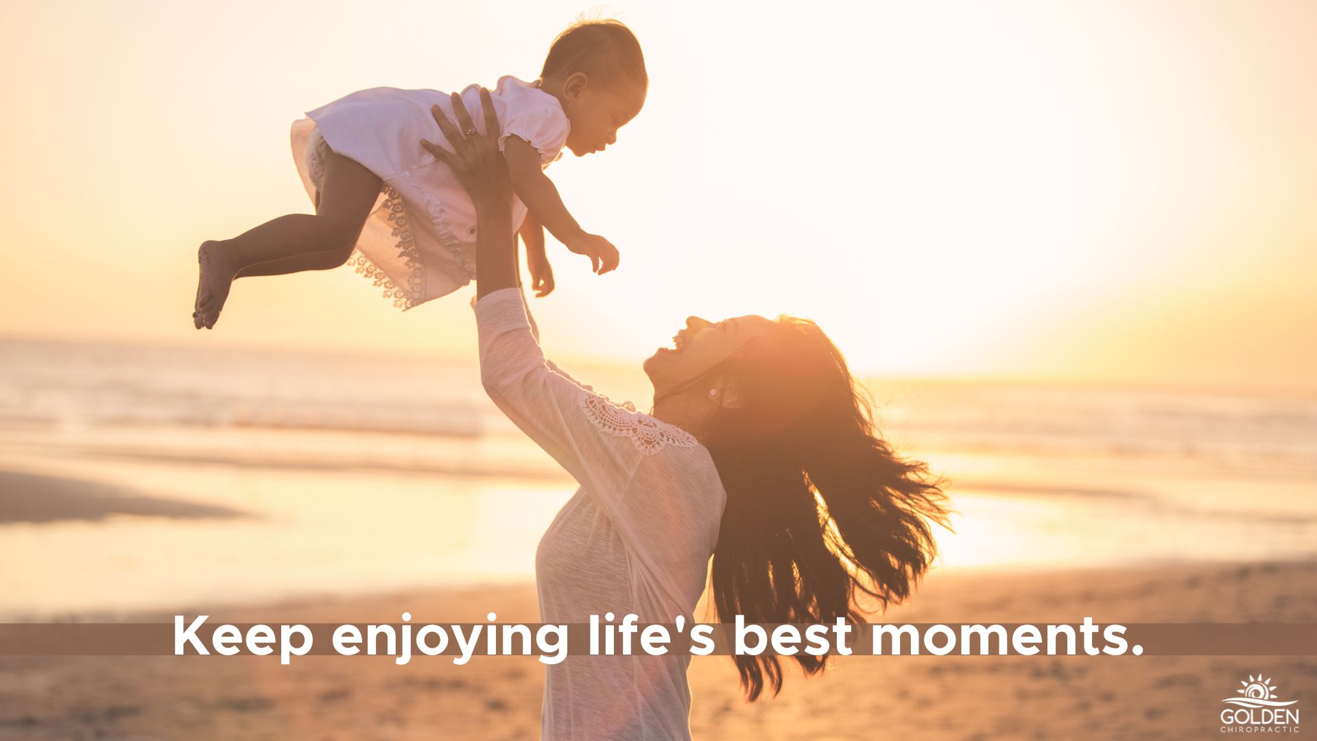 woman joyfully lifting her baby on the beach at sunset