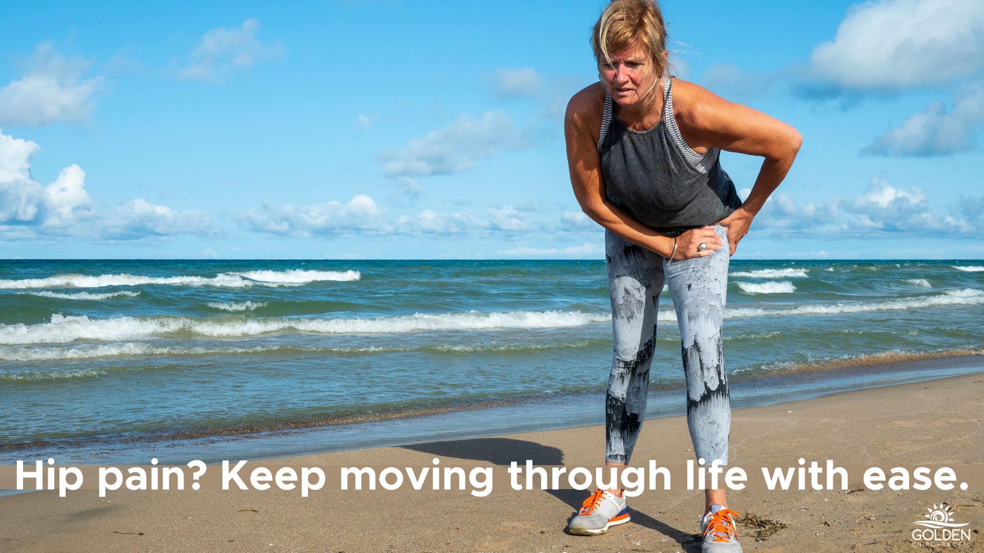 Older woman in workout clothes on the beach, clutching her hip in pain